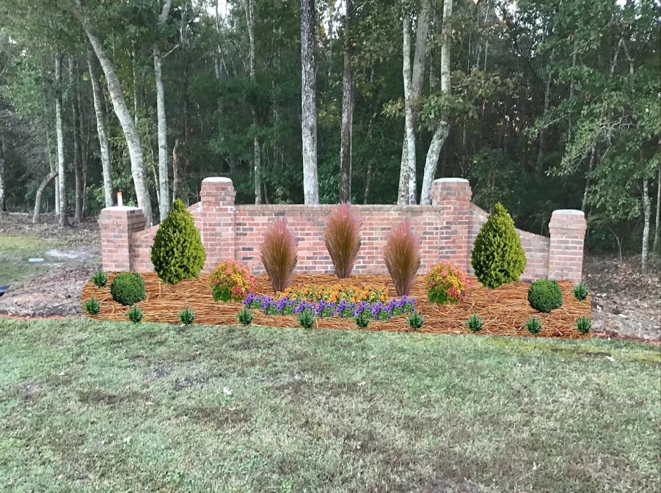 Brick retaining wall with ornamental grasses and flowering plants in front of evergreen forest