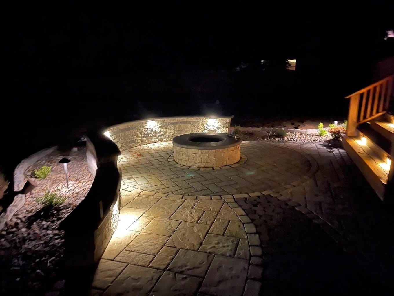 Nighttime backyard patio with illuminated stone seating wall and circular fire pit
