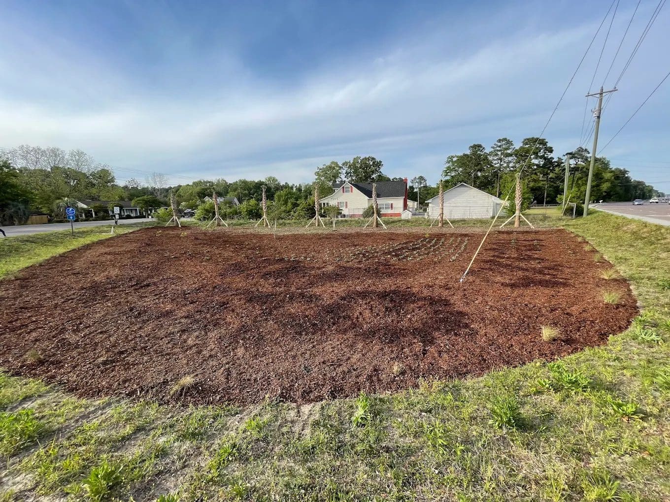 Freshly tilled brown soil in large garden plot with wooden support structures and residential houses in background