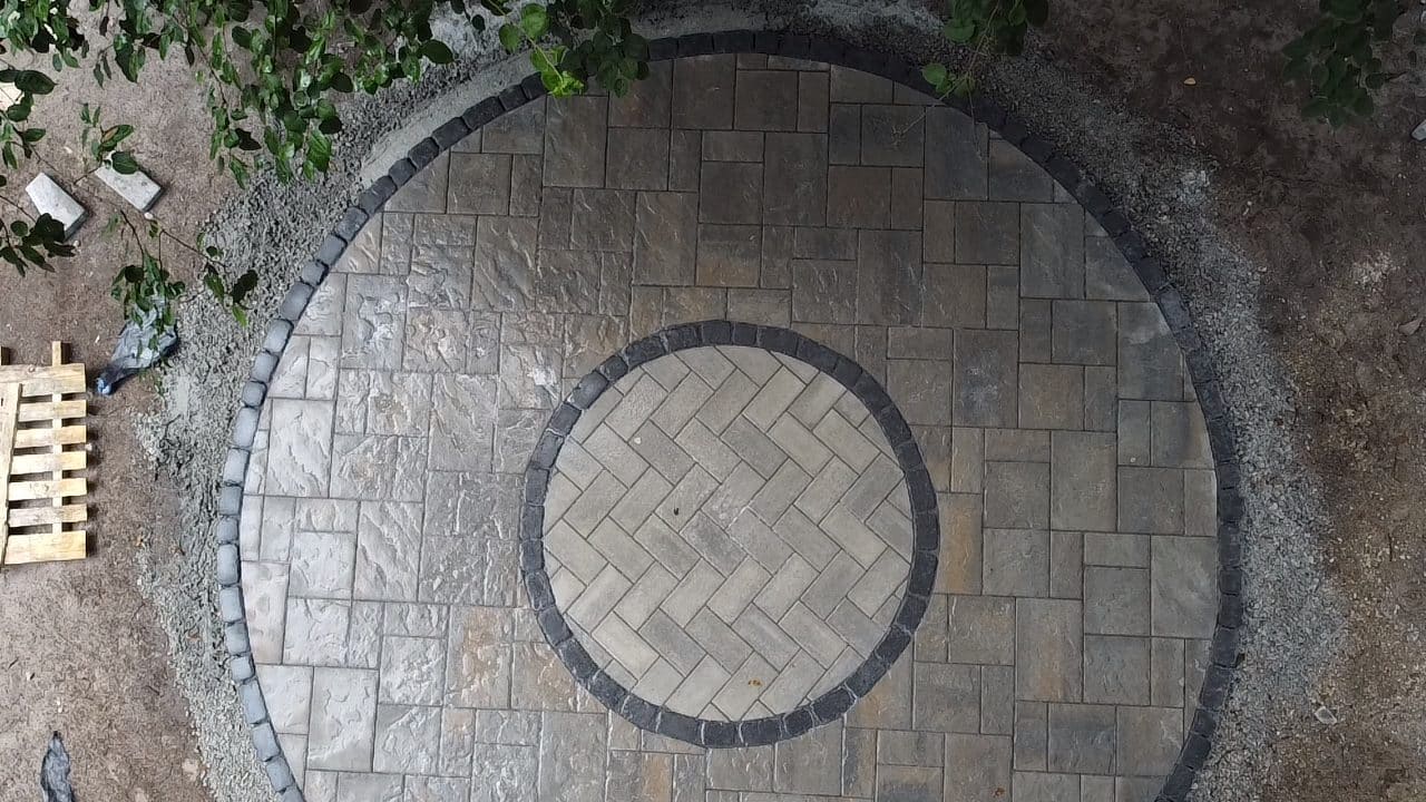 Circular paver patio with herringbone center pattern and dark border edging during installation