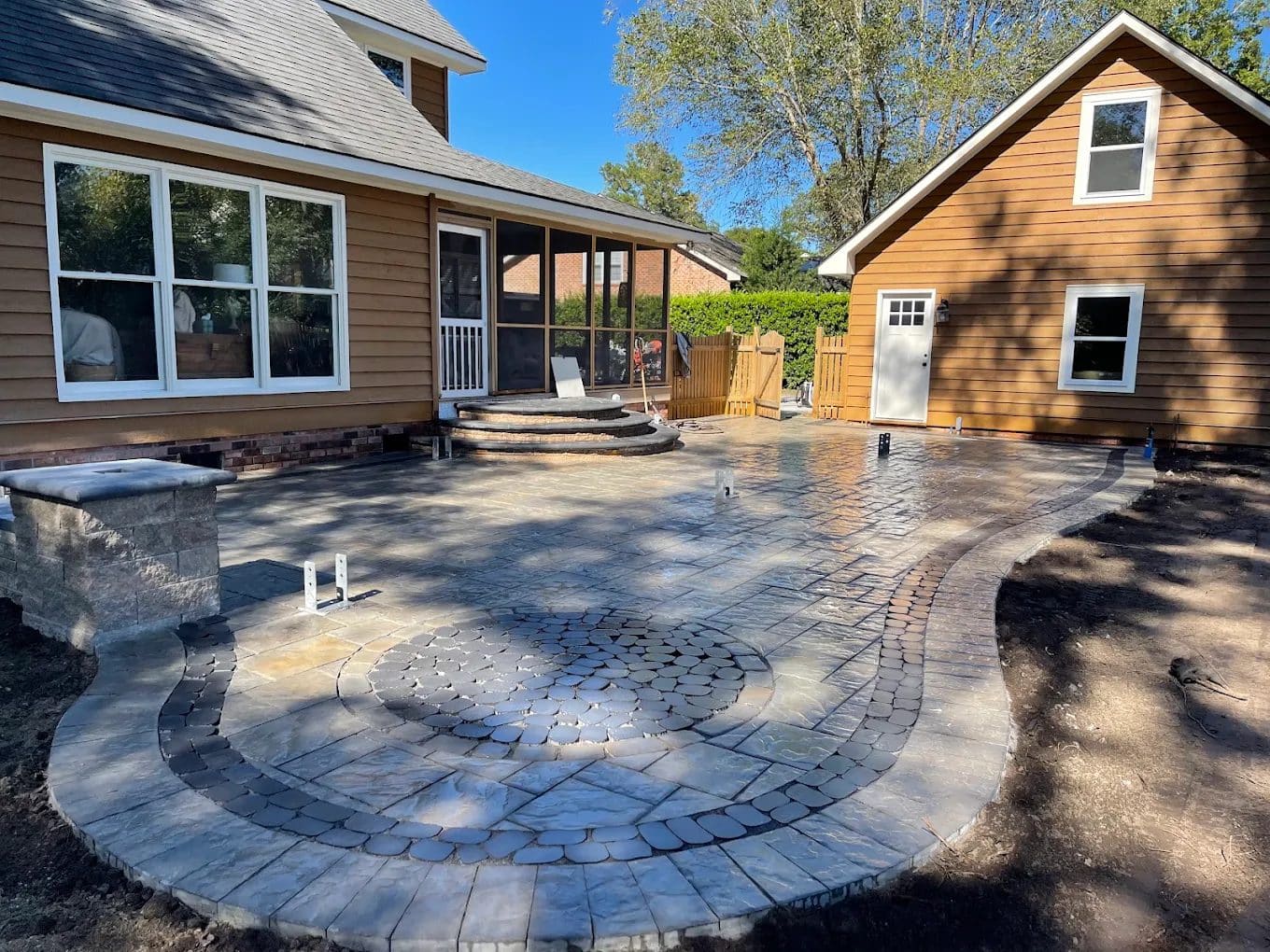 Paver patio with circular fire pit design in backyard with houses and screened porch