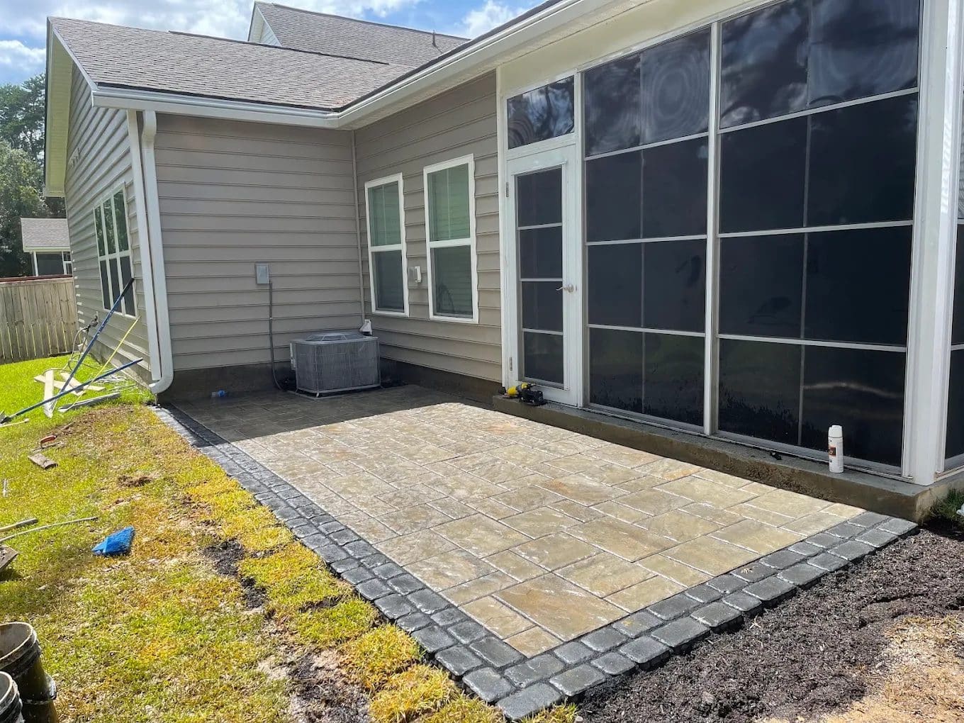 Backyard patio with pavers and black border, screened porch, tan siding house