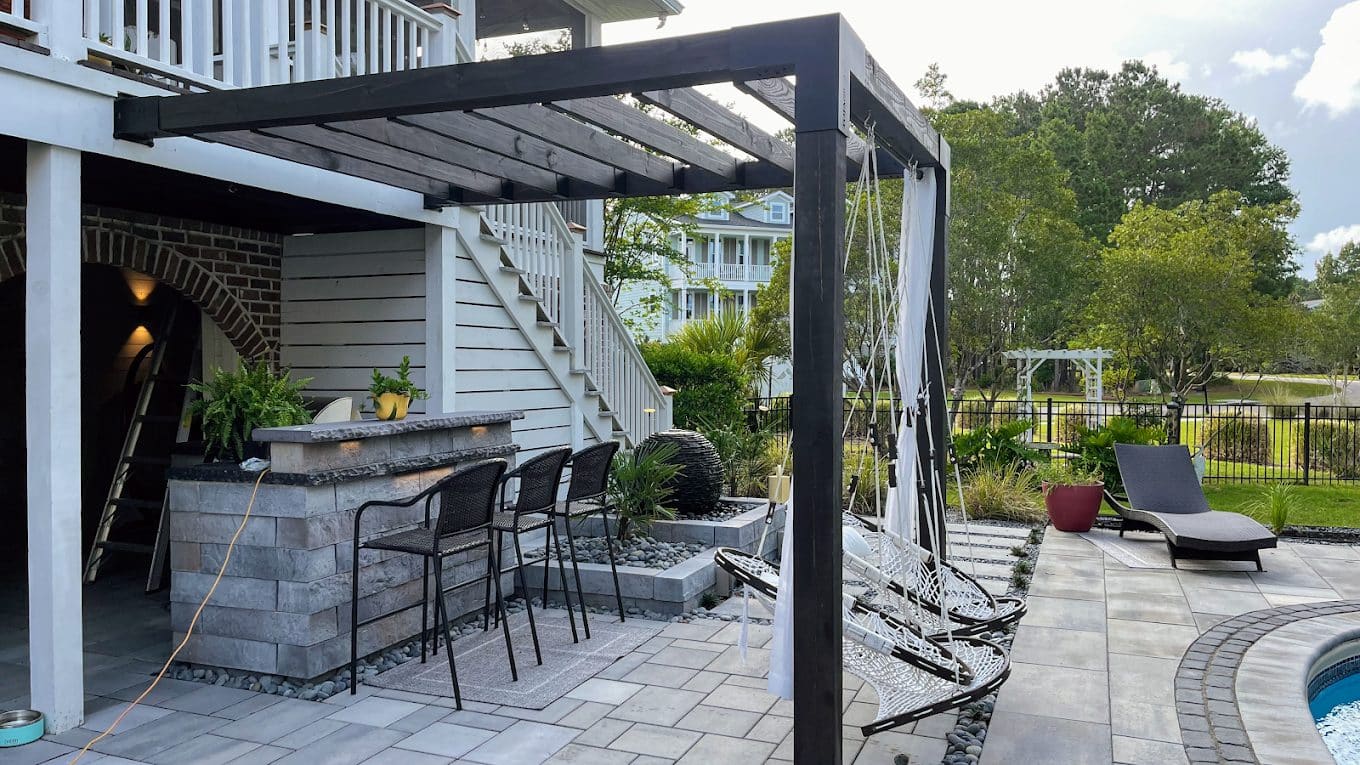 Modern backyard patio with black pergola, outdoor kitchen, lounge chairs, and pool area