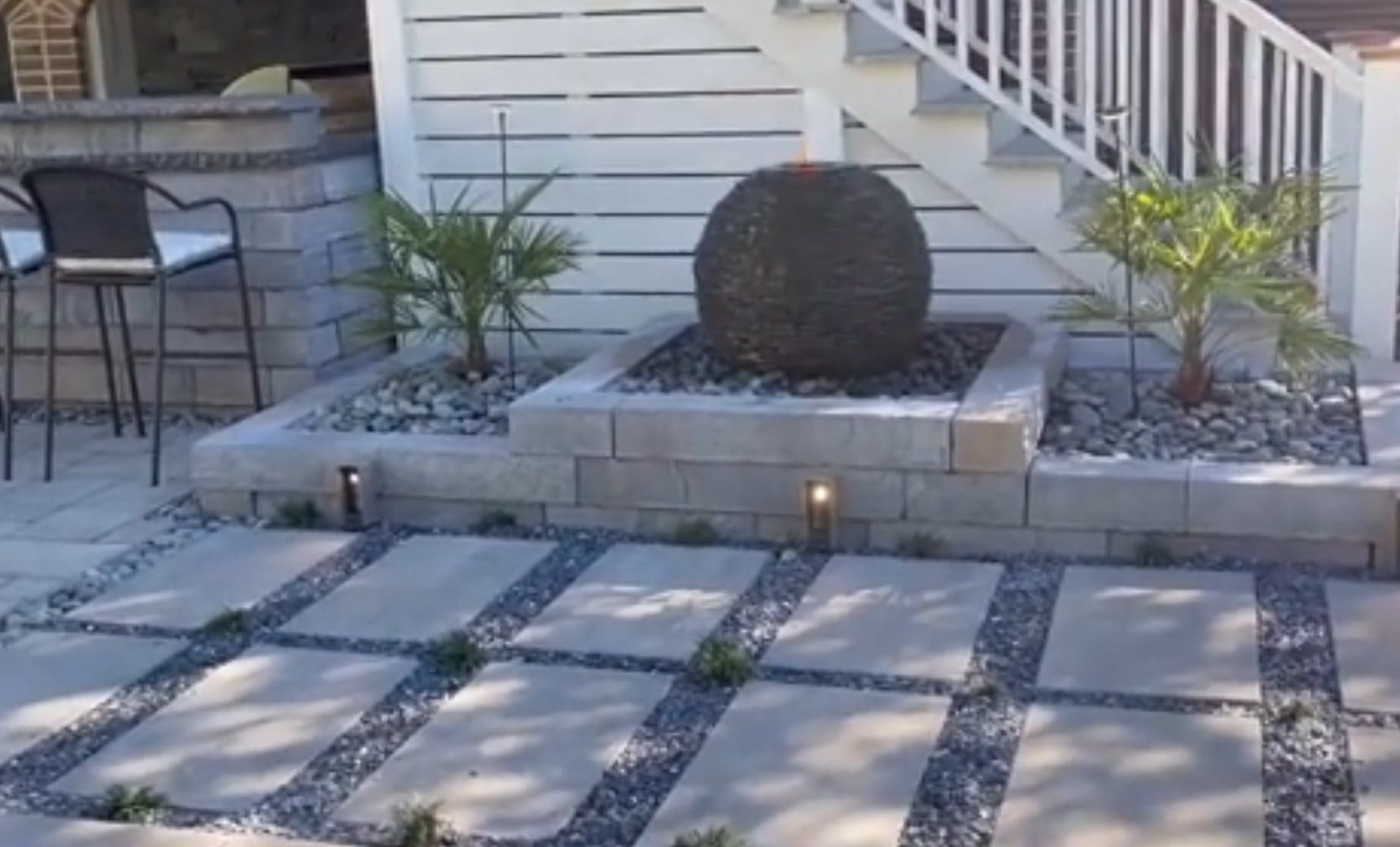 Modern patio with stepping stones, gravel pathways, raised planter beds, and a large dark sphere water feature