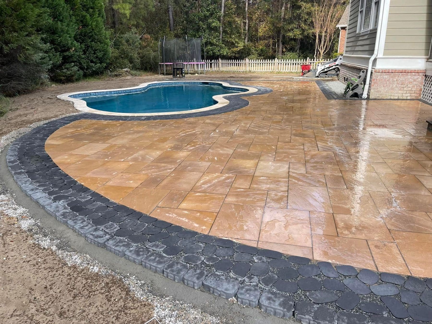 Newly installed patio with tan pavers and dark border edging surrounding an in-ground swimming pool