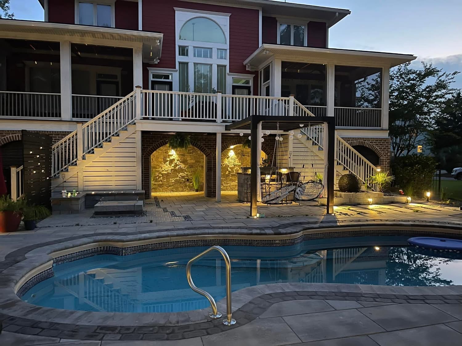 Modern home with illuminated patio, pool, and spa at dusk with mountains visible