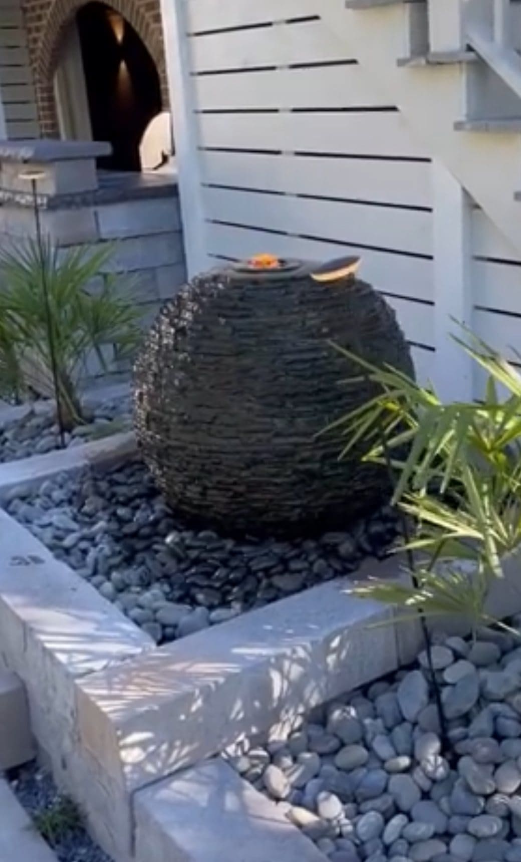 Woven black spherical water feature with flame accent in modern courtyard garden bed