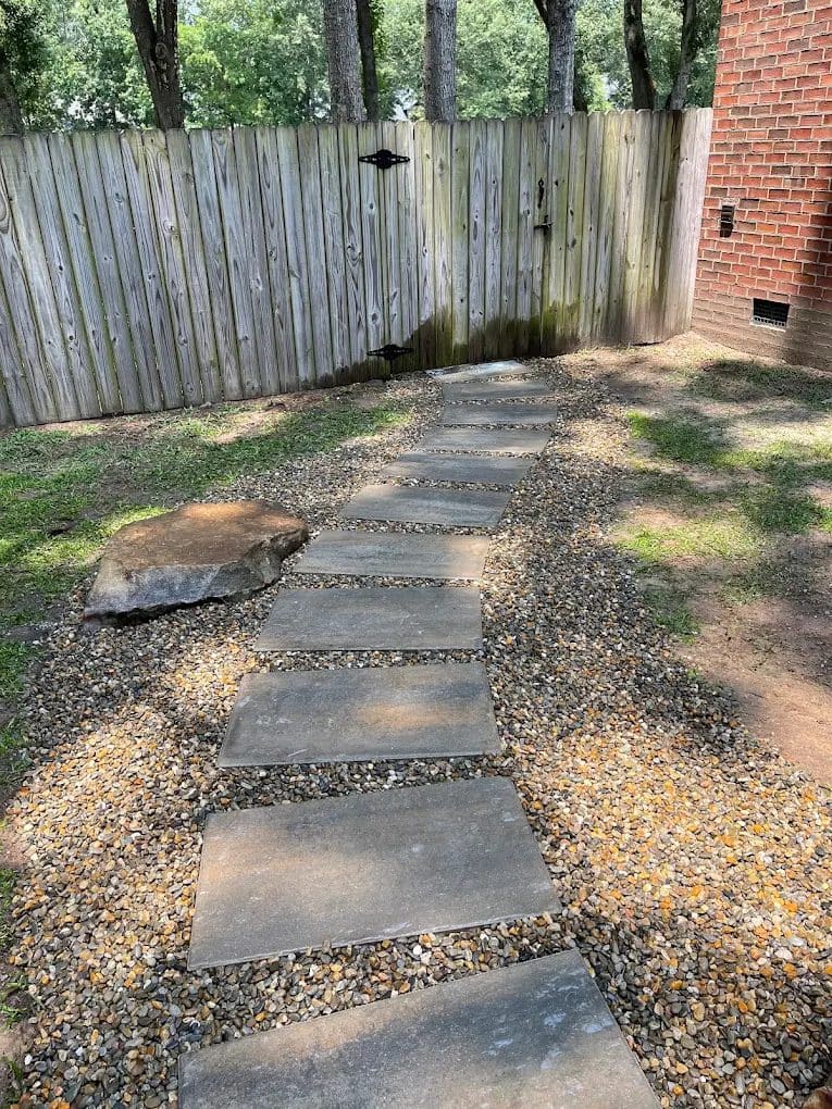 Stepping stone pathway through gravel leading to wooden gate and brick building