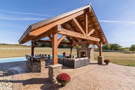 Large wooden pavilion with fireplace and outdoor seating area on stamped concrete patio